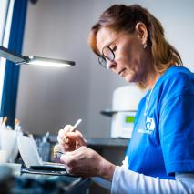 Zahntechnikerin bearbeitet Zahnersatz konzentriert unter Arbeitslampe.