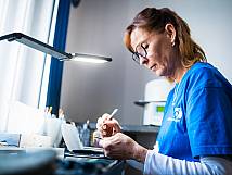 Zahntechnikerin bearbeitet Zahnersatz konzentriert unter Arbeitslampe.